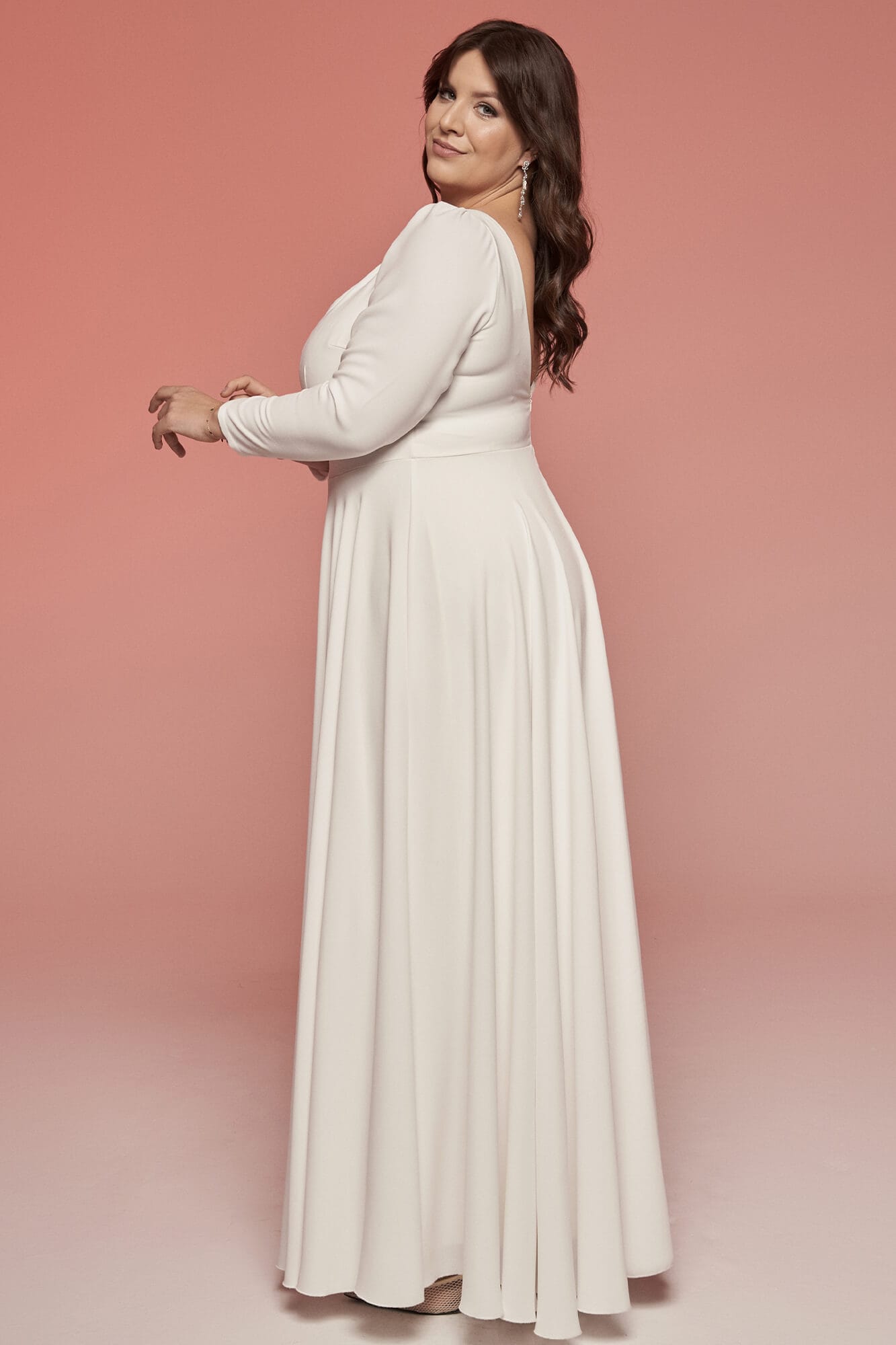 suknia ślubna o długim rękawie i luźnym kroju, w kolorze białym, prezentowana na tle różowym
