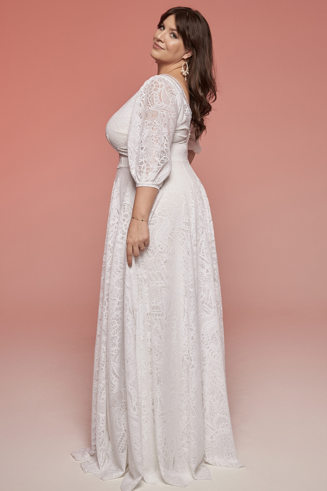 suknia ślubna z długim rękawem i koronkowym wykończeniem, na tle różowego tła