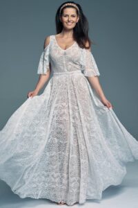 Suknia ślubna z koronkowym wzorem, z rękawami w kształcie dzwonu i rozkloszowanym dołem.