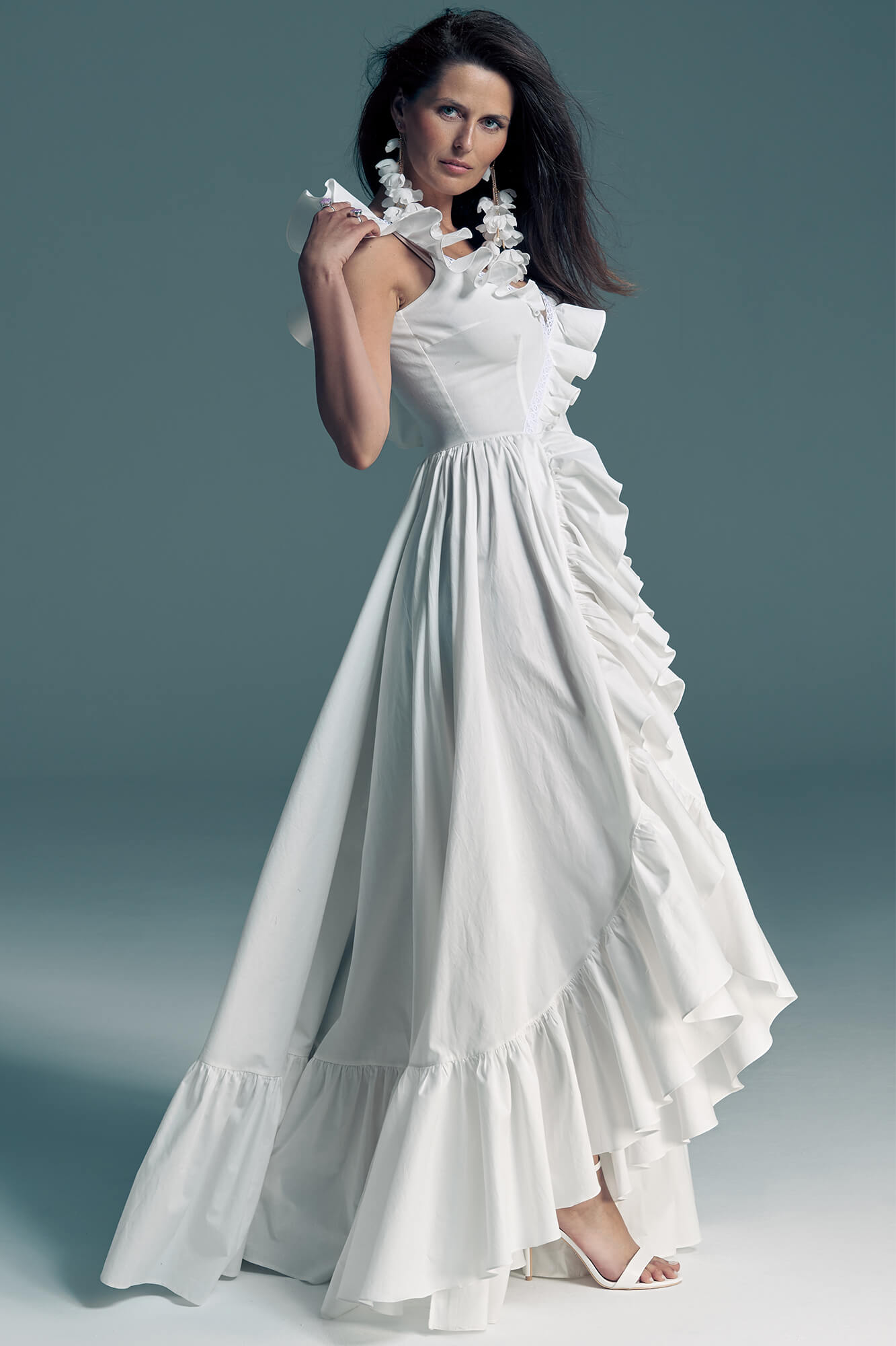 suknia ślubna z falbanami, bez rękawów, w kolorze białym, na modelce stojącej na szarym tle