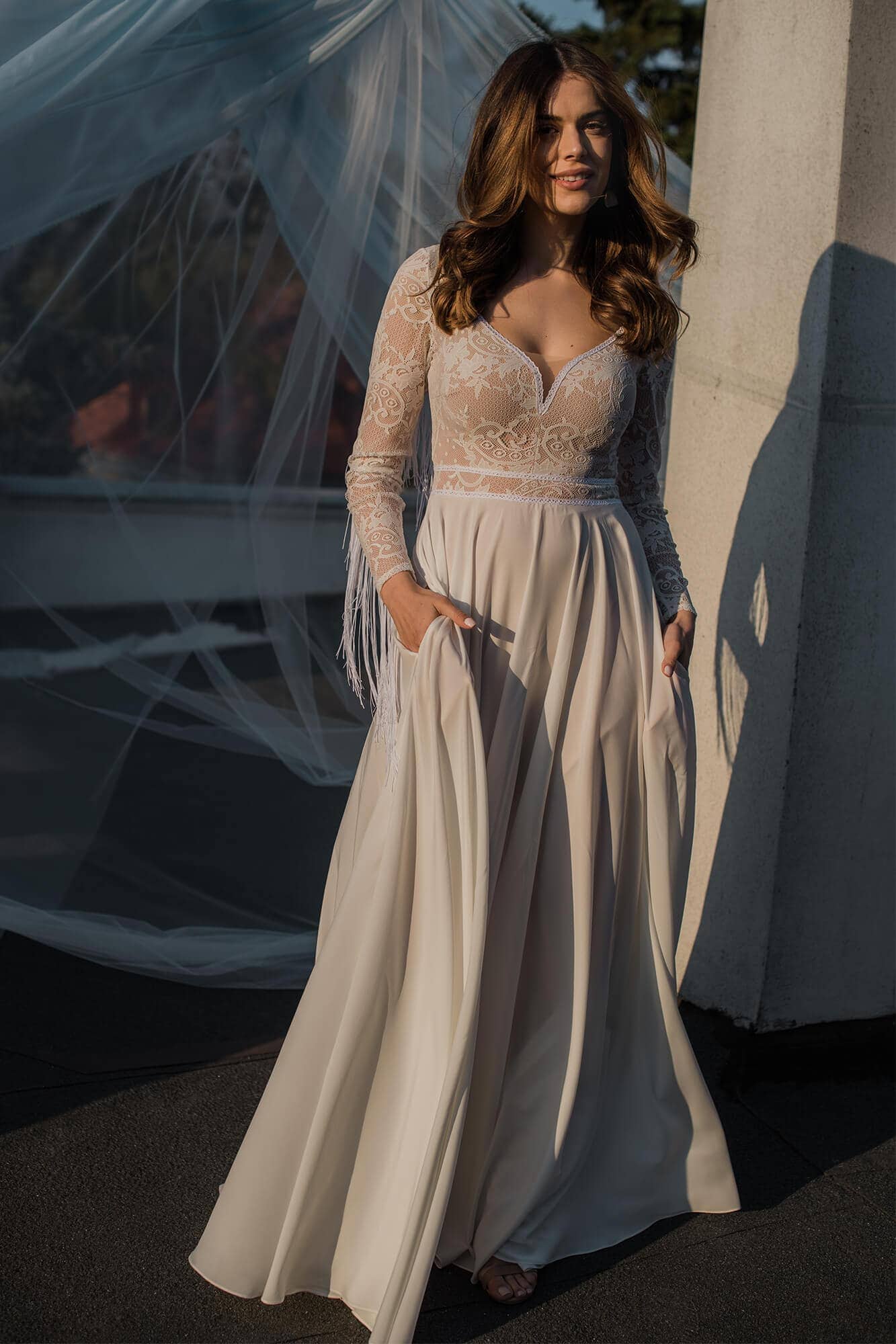 Suknia ślubna z długimi rękawami, koronkowym dekoltem i luźnym dołem.