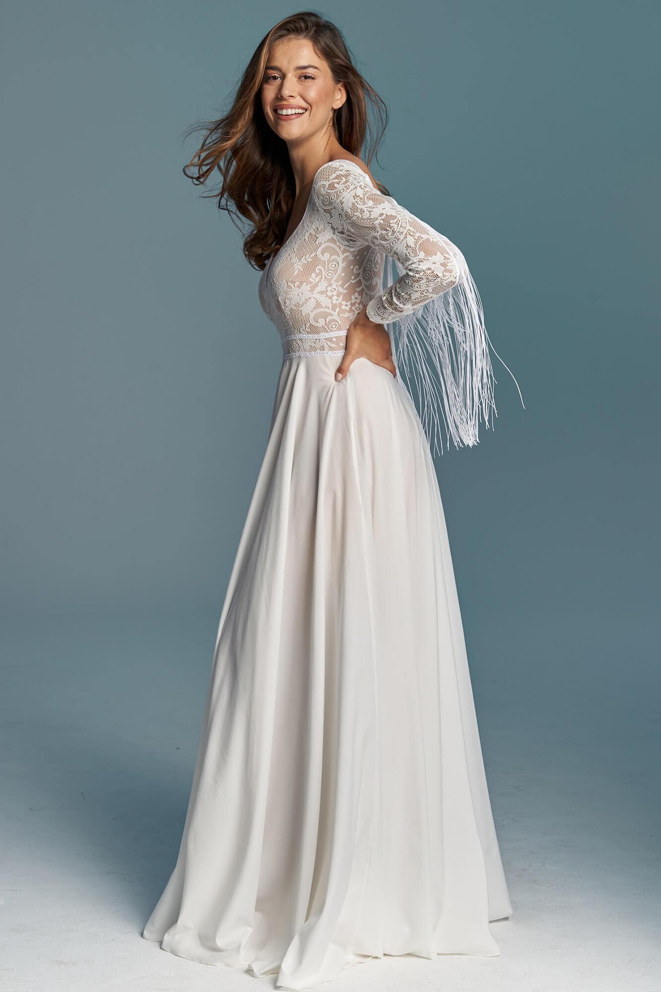 suknia ślubna z długimi koronkowymi rękawami i frędzlami, w kolorze białym.
