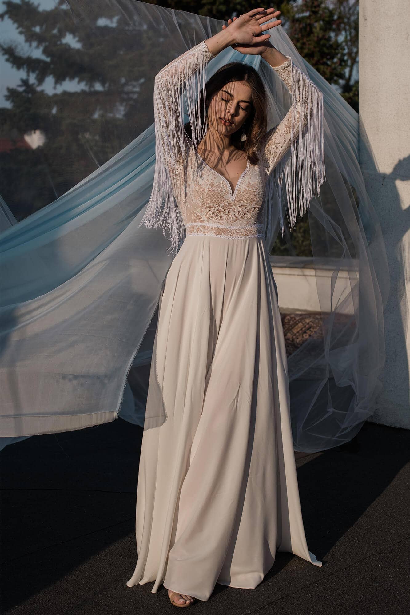 suknia ślubna z koronkowym górnym fasonem i długimi rękawami, z tiulowym welonem w tle