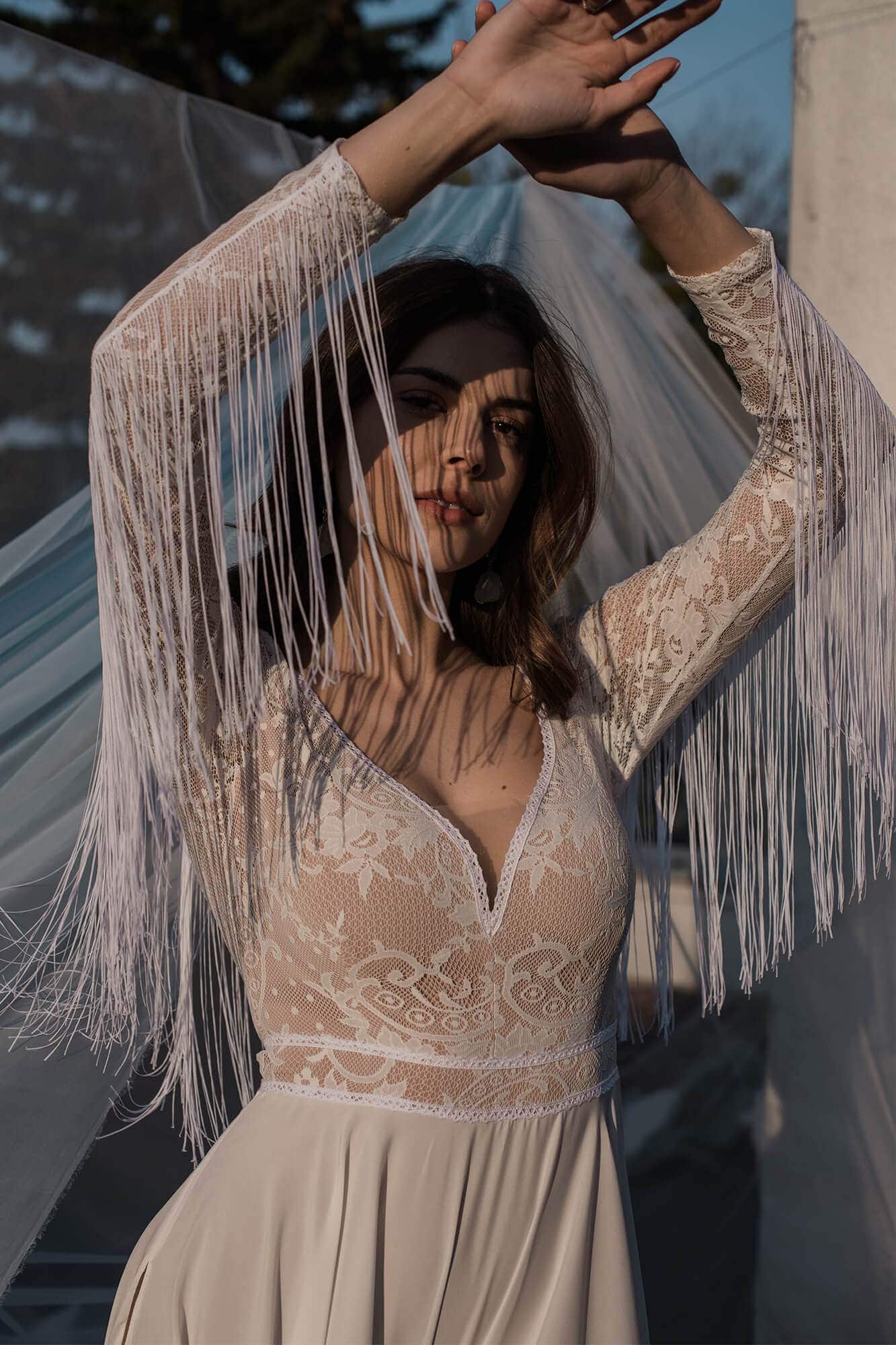 Suknia ślubna z koronkowym górnym fragmentem i frędzlami na rękawach.