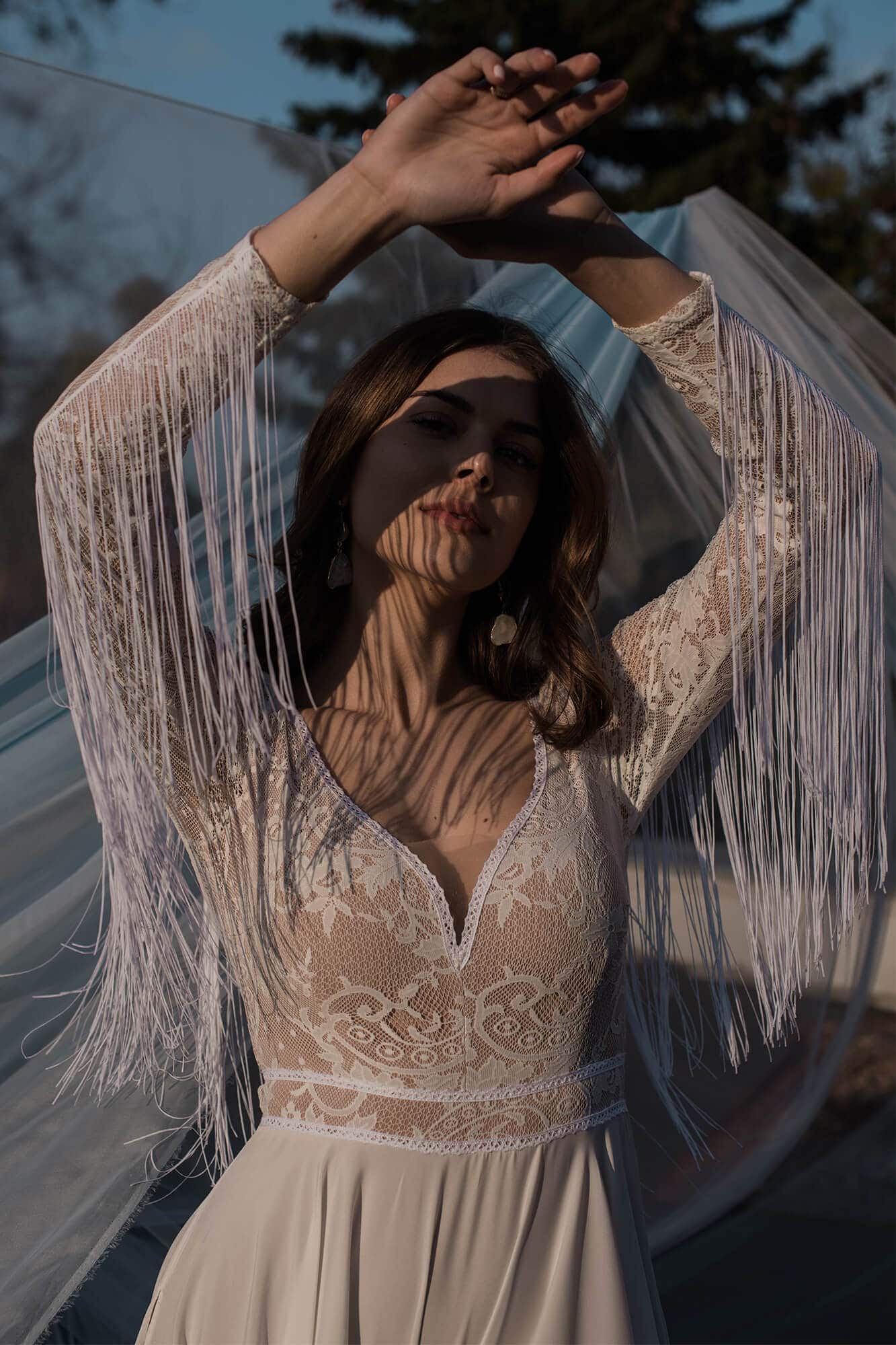 suknia ślubna z koronkowym wykończeniem i frędzlami na rękawach, prezentowana przez kobietę.