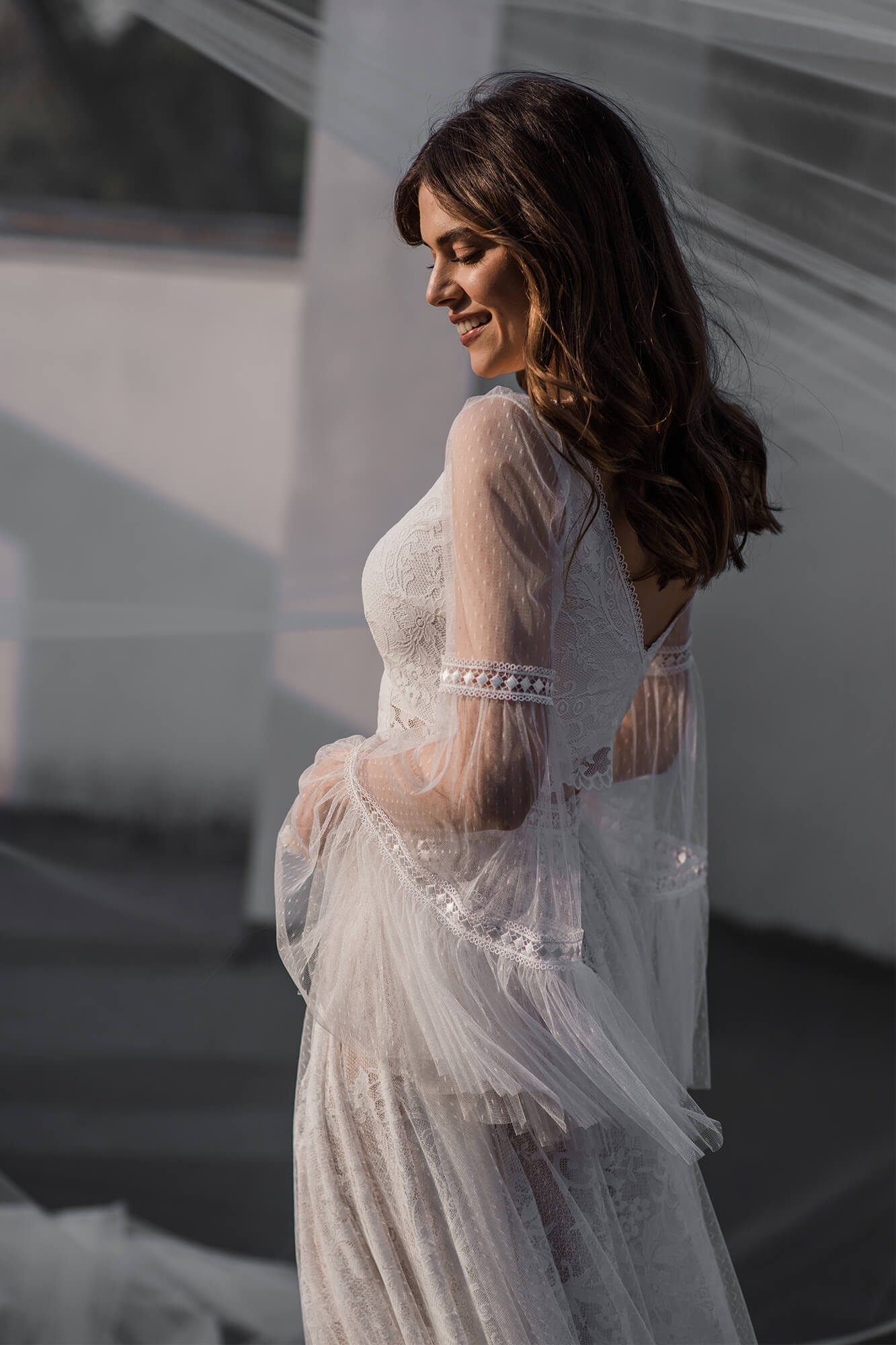 suknia ślubna z długimi rękawami i koronkowymi detalami, modelka w białej sukni na tle jasnej ściany