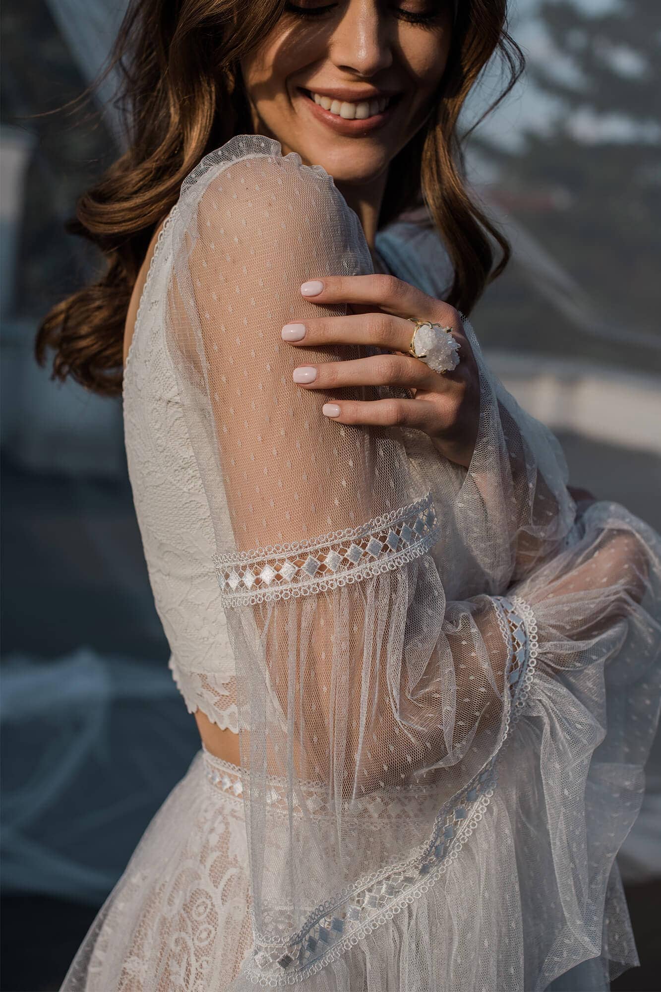 Suknia ślubna z długimi, przezroczystymi rękawami i koronkowymi detalami.