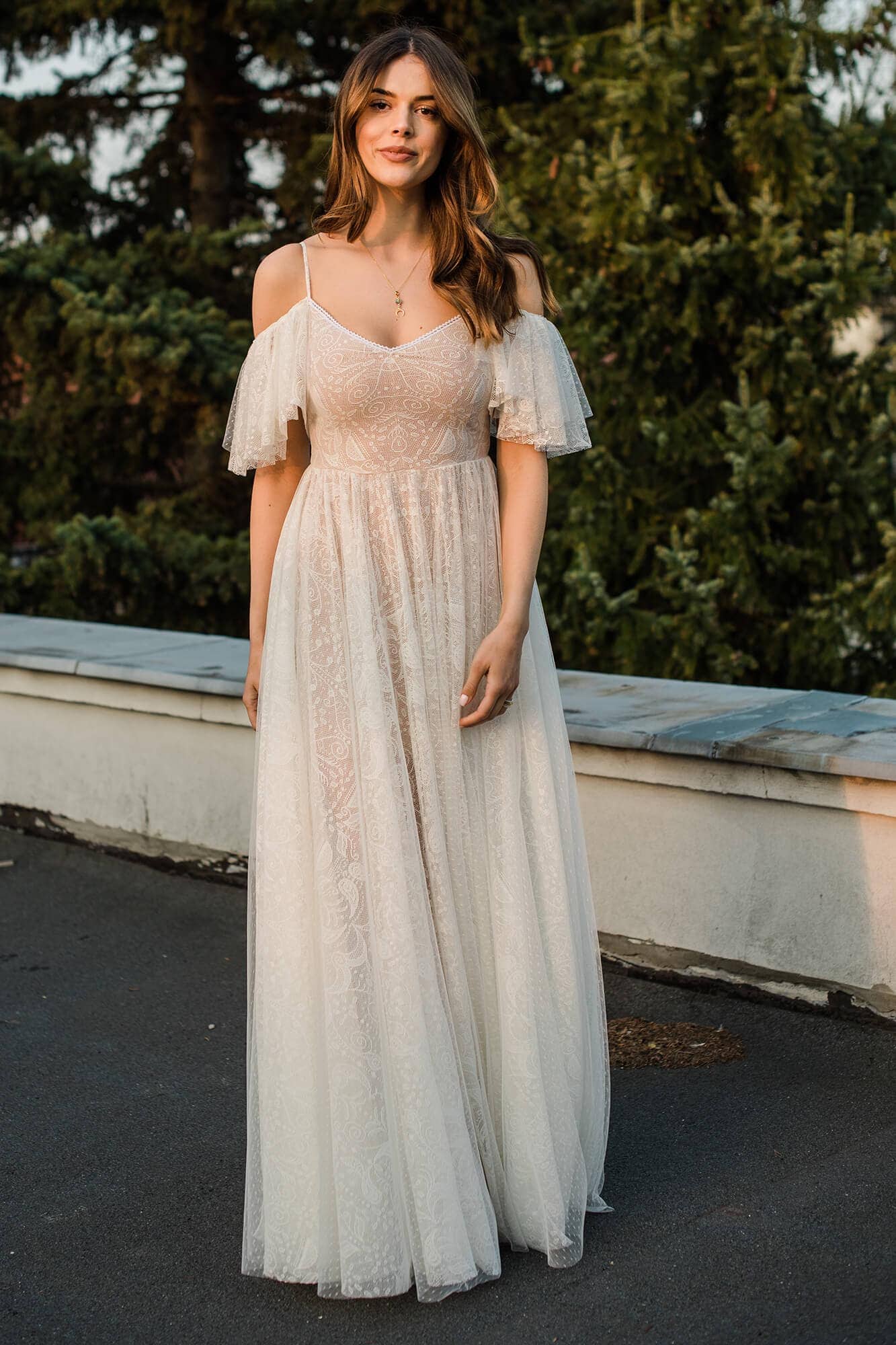 suknia ślubna z koronkowymi rękawami i długim dołem, modelka stoi na tle zieleni