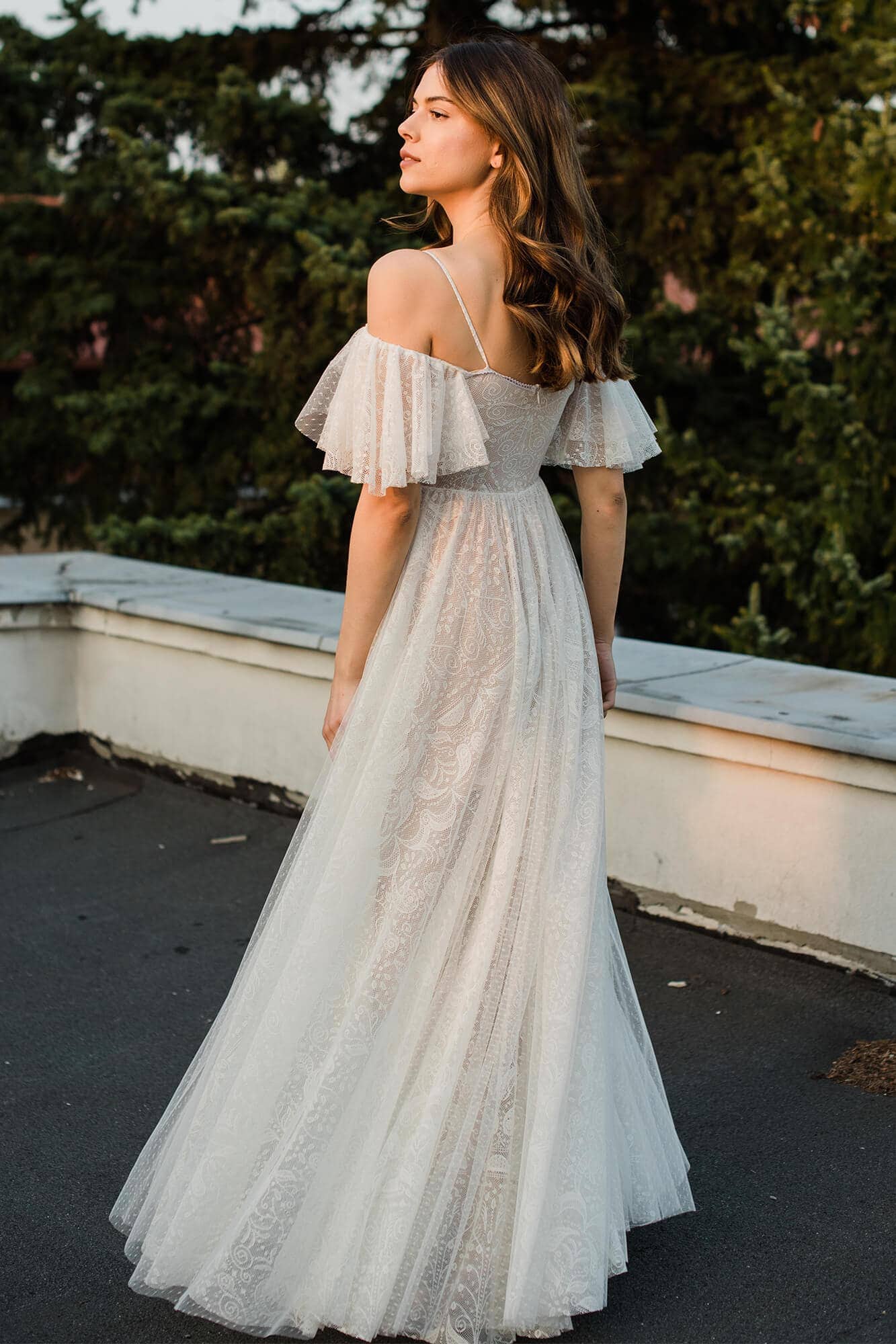 Suknia ślubna z odkrytymi ramionami i falbaniastymi rękawami, z długim, zwiewnym dołem.
