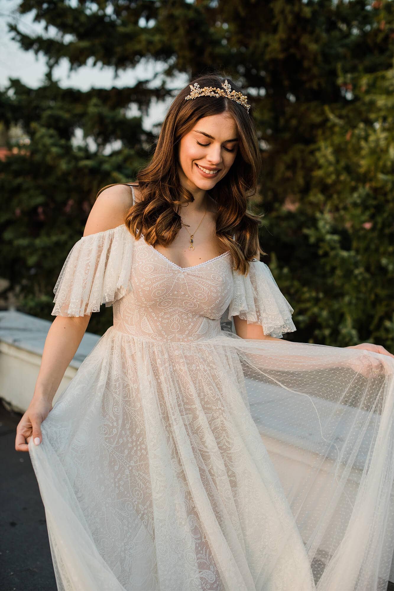 suknia ślubna z odkrytymi ramionami i falbanami, w jasnym kolorze z ozdobnymi detalami.