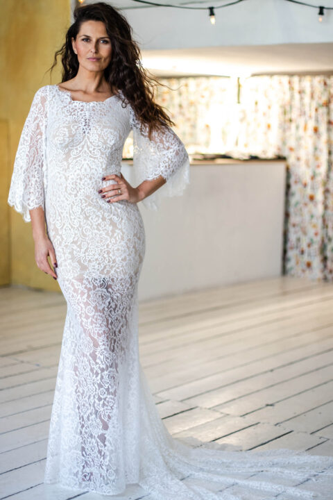 suknia ślubna z koronkowym wykończeniem i długimi rękawami, modelka stoi na drewnianej podłodze