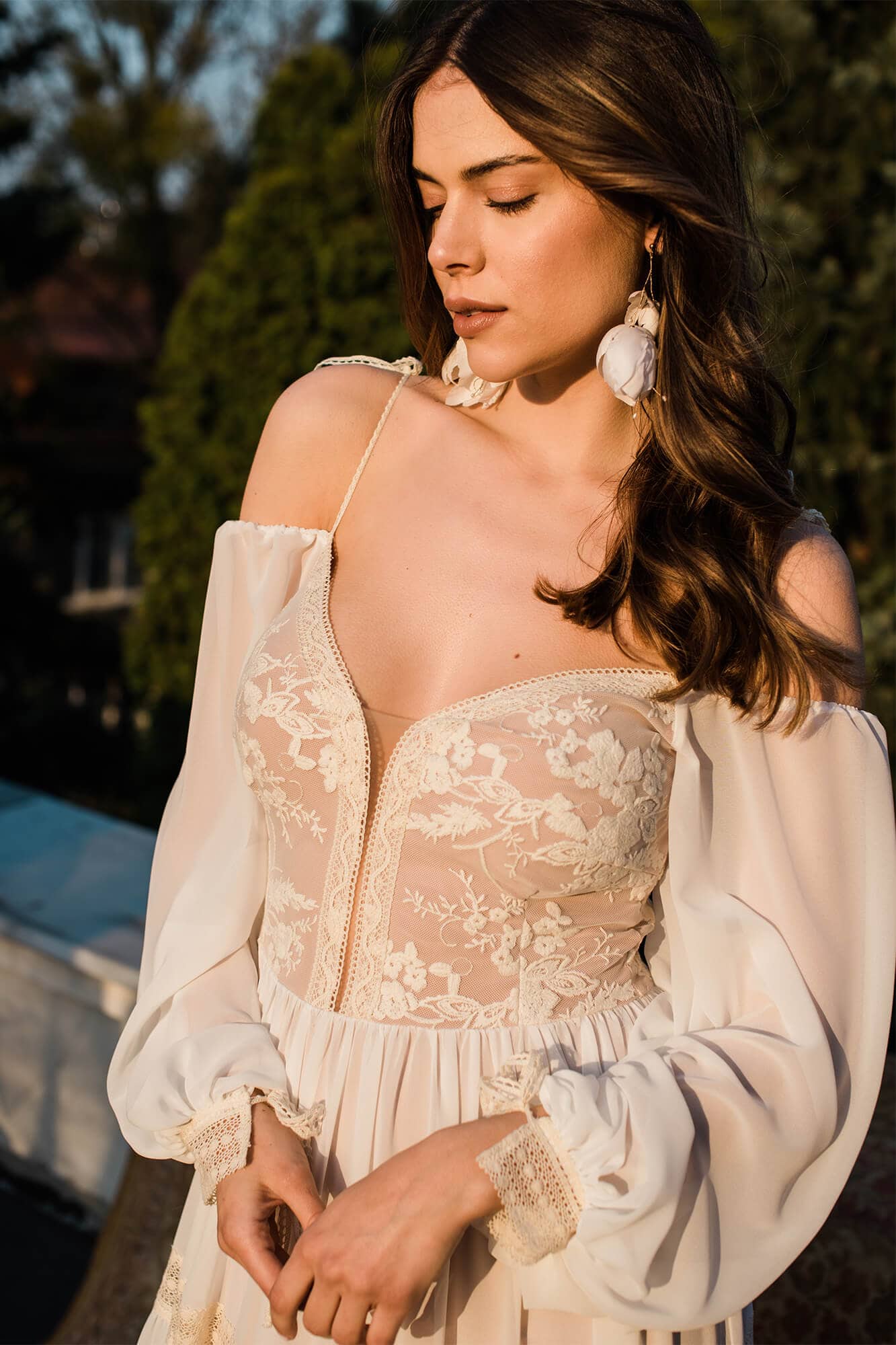 suknia ślubna z koronkowym gorsetem i długimi rękawami, modelka z biżuterią na uszach