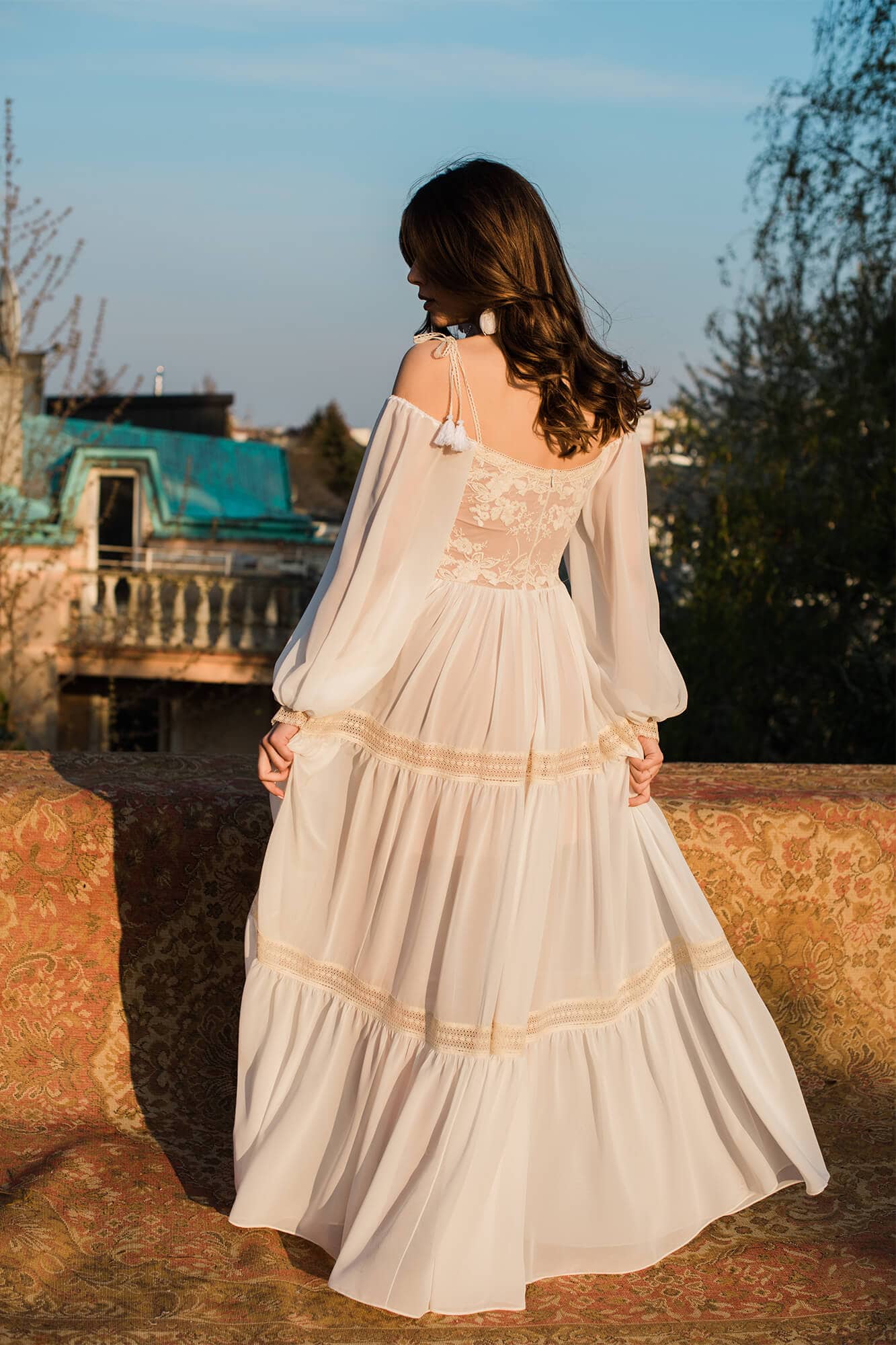 Suknia ślubna z długimi rękawami, z falbanami i koronkowym wykończeniem, widoczna z tyłu.