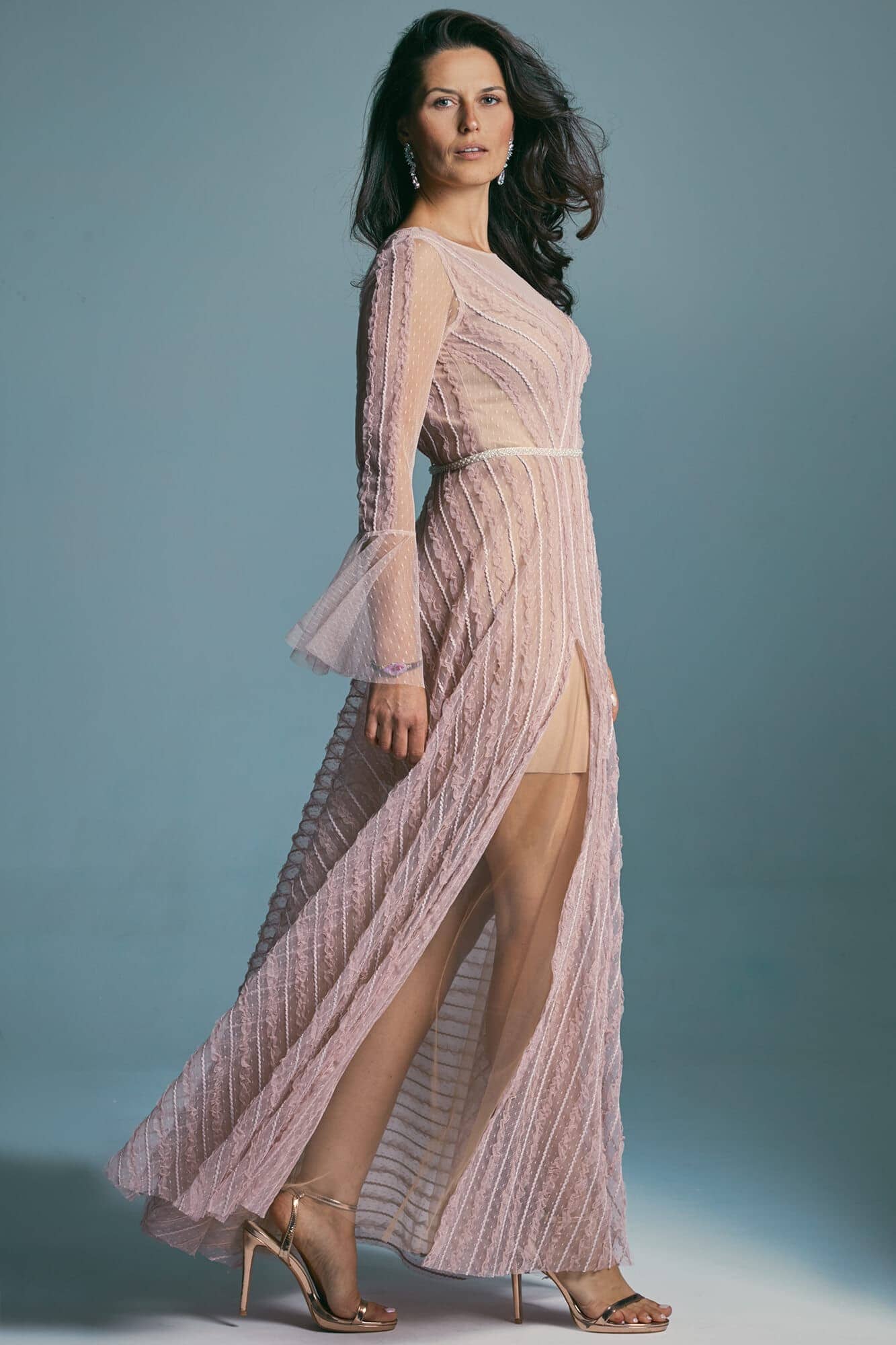 suknia w kolorze różowym z długimi rękawami i rozcięciem na nodze, modelka w szpilkach na tle niebieskim