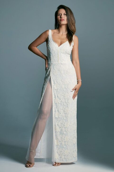 suknia ślubna z koronkowym wykończeniem i rozcięciem z boku, modelka w białej sukni na szarym tle