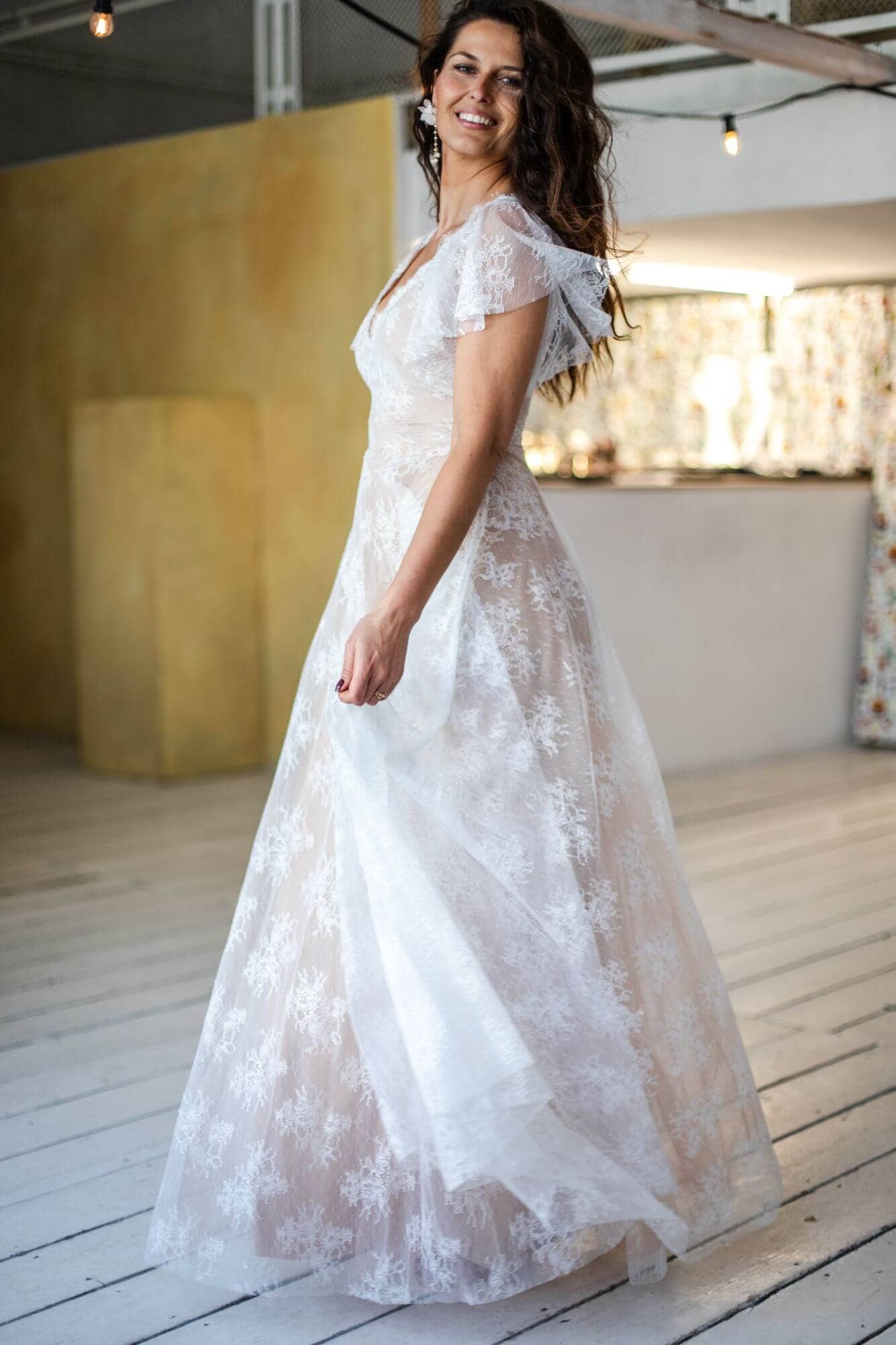 suknia ślubna z koronkowymi detalami i rękawami, prezentowana na modelce w jasnym wnętrzu