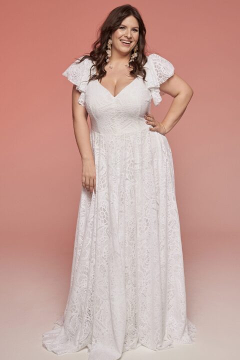 suknia ślubna z koronkowymi rękawami, w kolorze białym, na tle różowej ściany