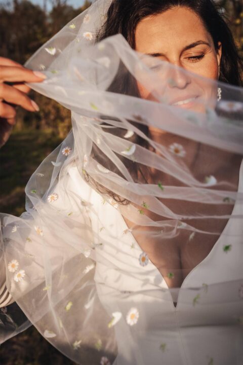 Kobieta w białej sukni ślubnej z przezroczystym welonem ozdobionym haftem.