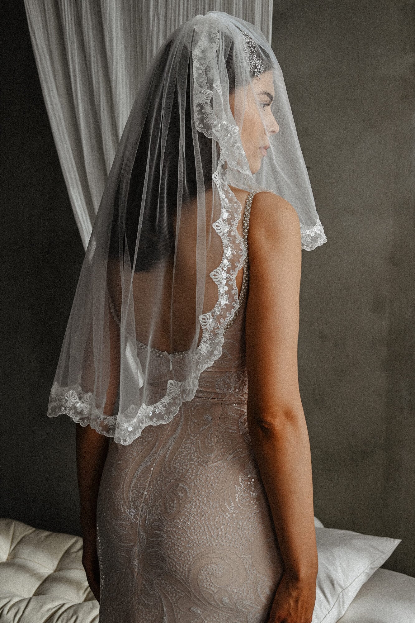 suknia ślubna z długim welonem, widoczna z tyłu, na tle szarej ściany
