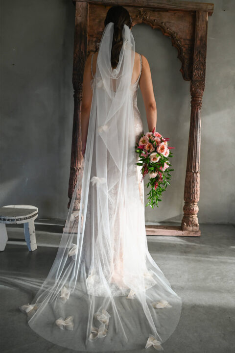 suknia ślubna z przezroczystego materiału, z dekoltem w serek, osoba trzymająca bukiet kwiatów