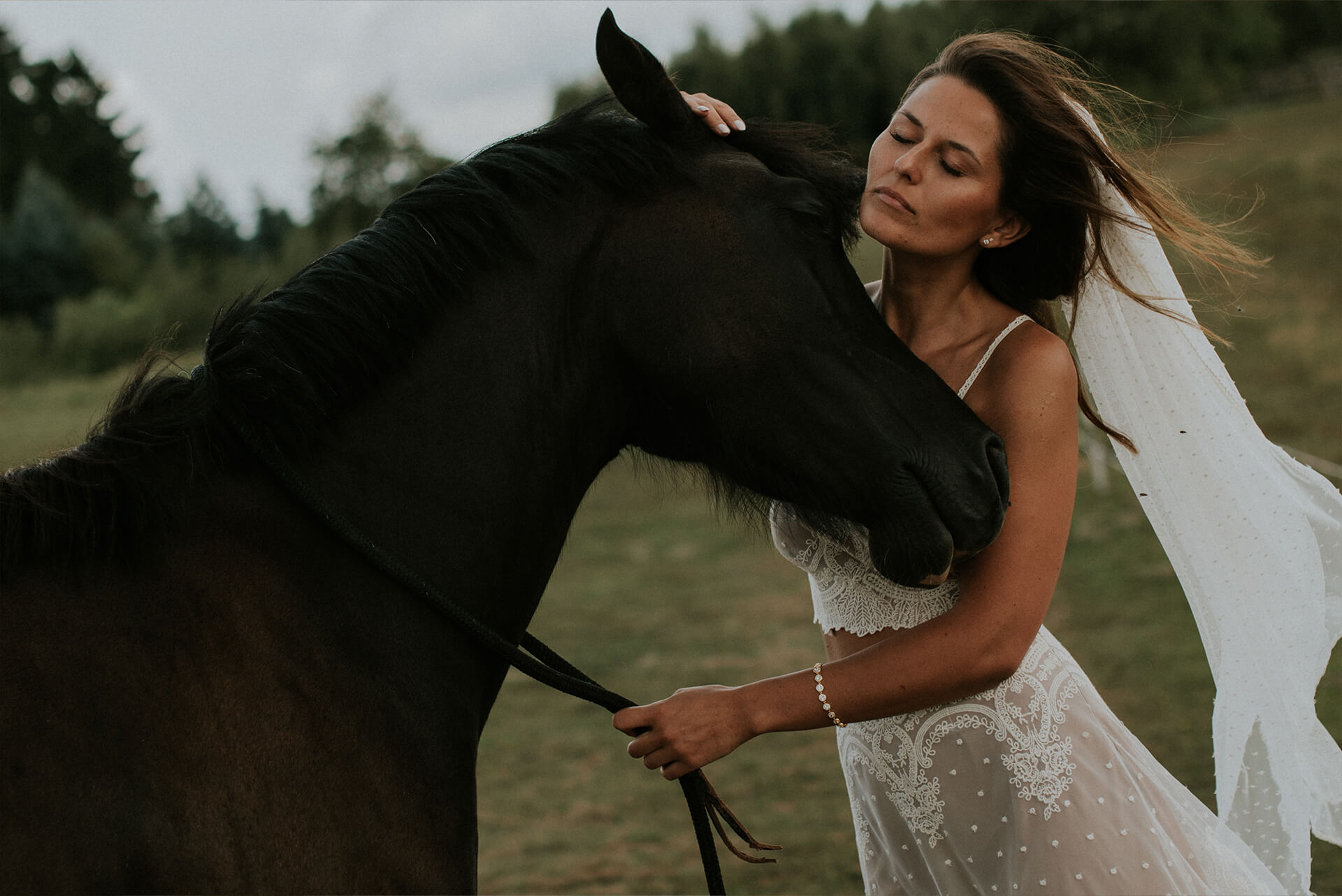 suknia ślubna z koronkowym wykończeniem, model z długim welonem, osoba trzymająca konia
