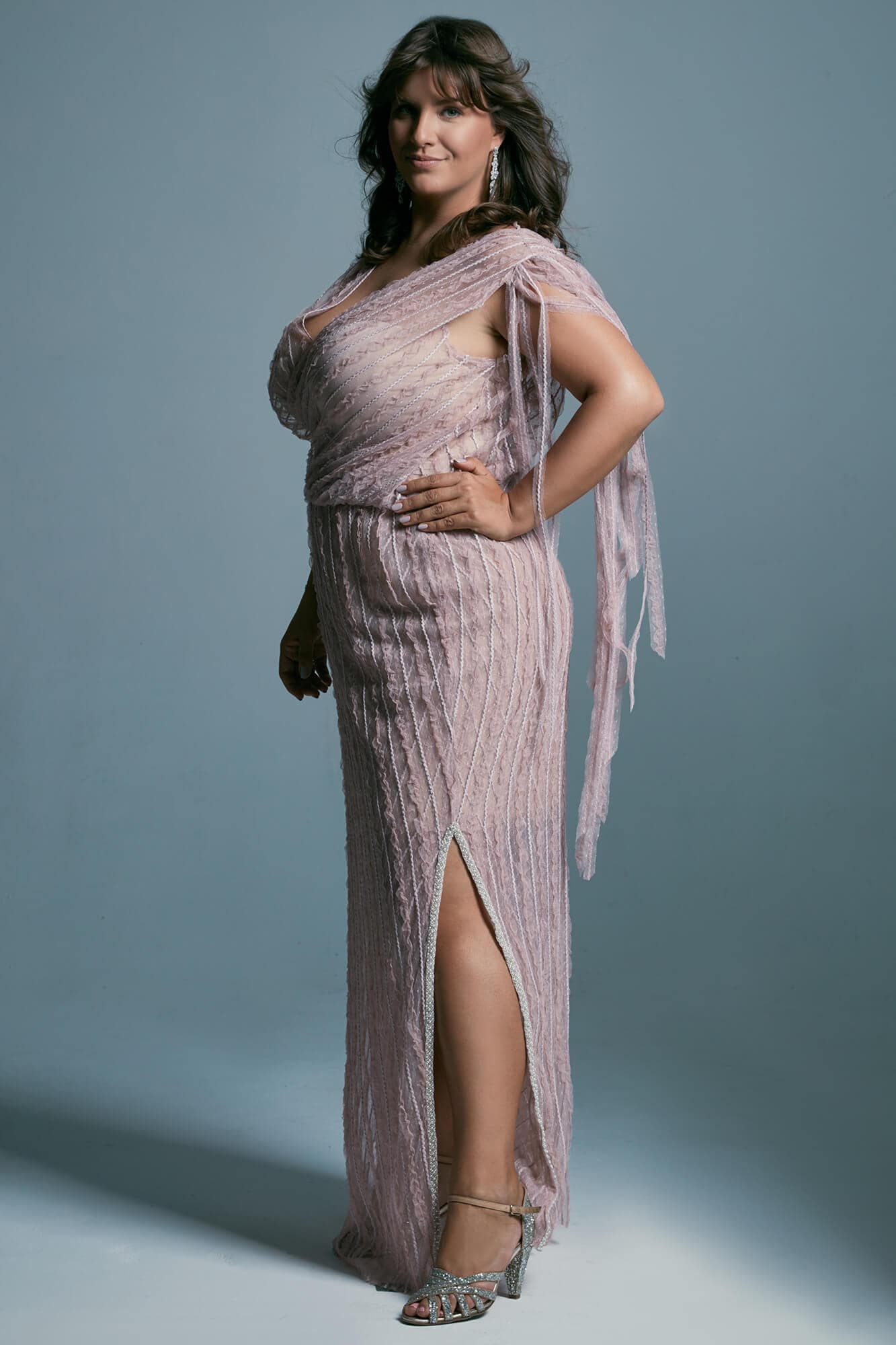 suknia w kolorze różowym z rozcięciem i drapowaniem, modelka stoi na tle niebieskiej ściany