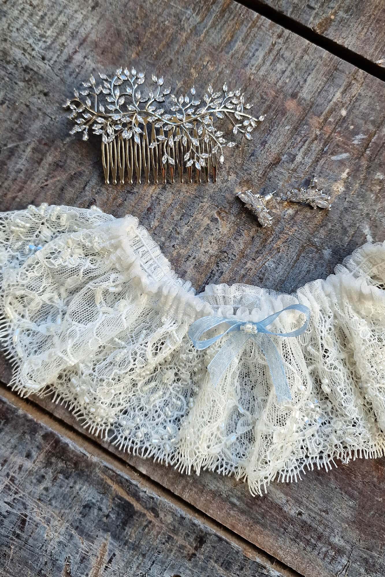 Koronkowy pas do sukni ślubnej w kolorze kremowym leży na drewnianym stole obok suszonych kwiatów.