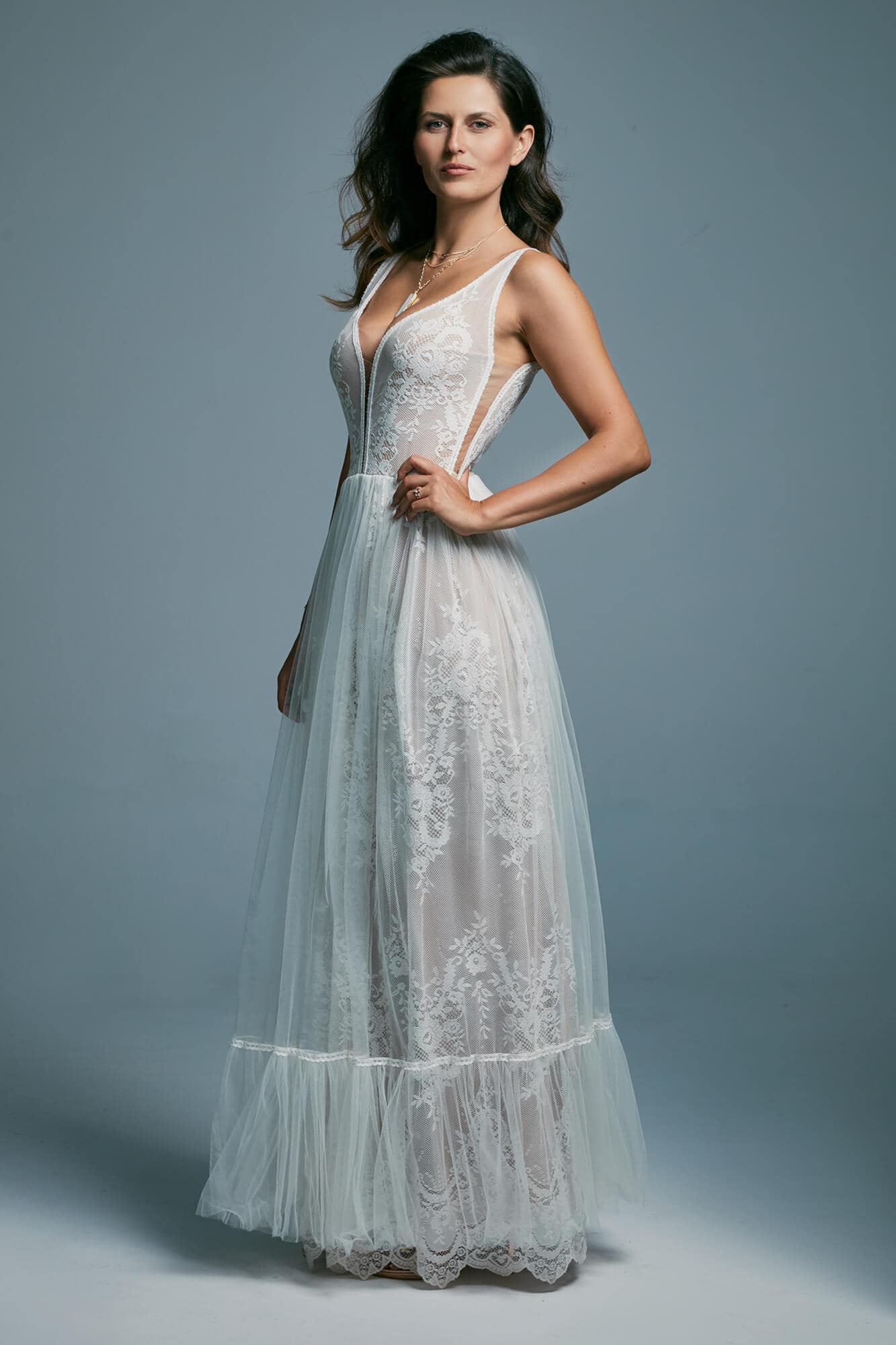 suknia ślubna z koronkowymi detalami i delikatnymi ramiączkami, modelka stoi na jednolitym tle