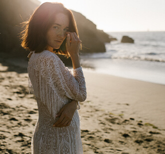 suknia ślubna z koronkowym wzorem, z długim rękawem, na tle plaży i morza