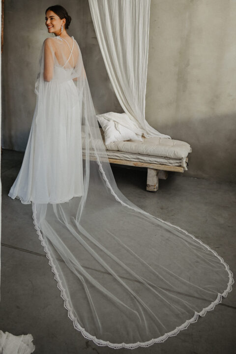 suknia ślubna z długim trenem i delikatnym welonem, modelka stoi na tle betonu