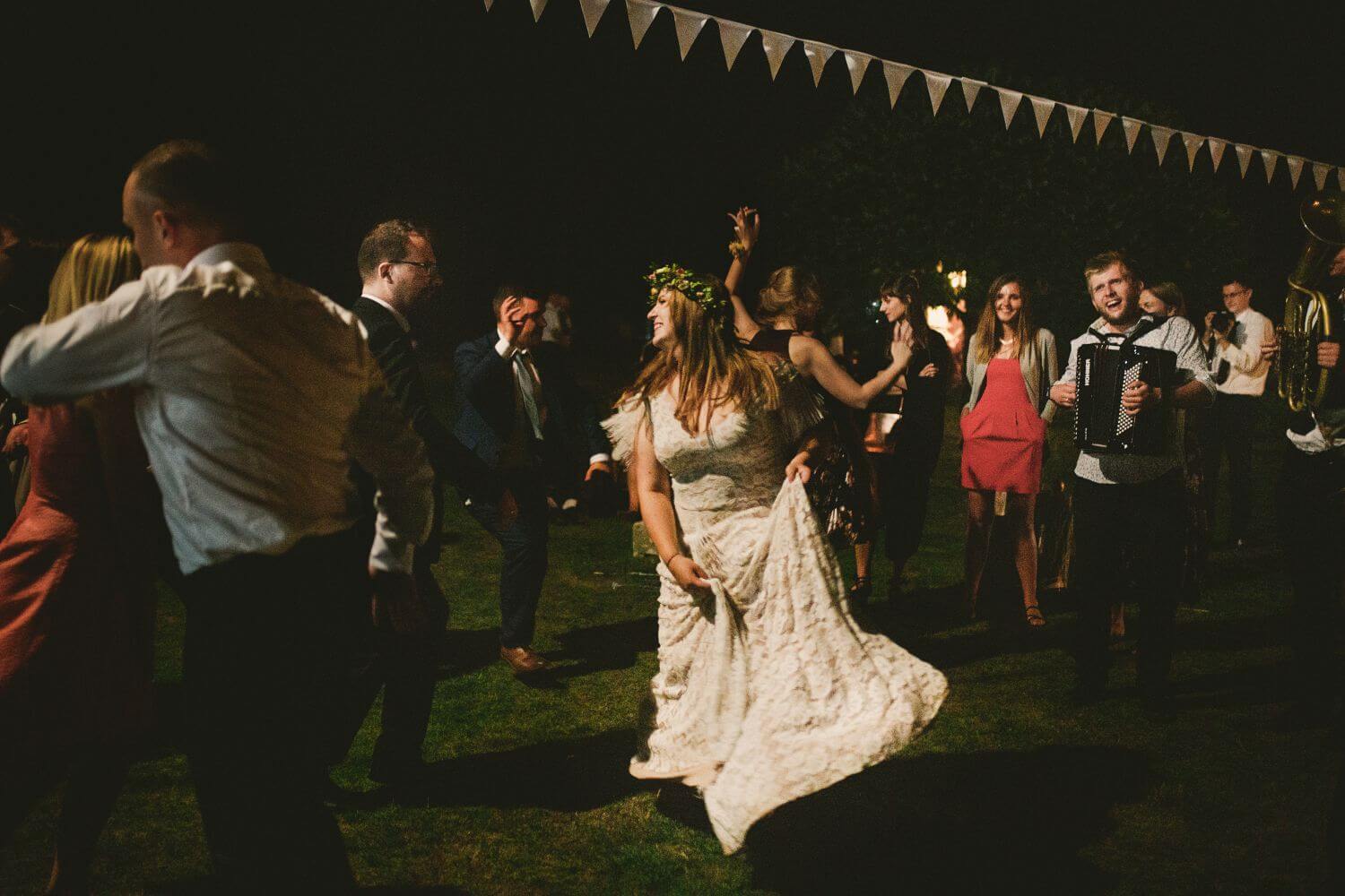 Osoba w sukni ślubnej tańczy na przyjęciu w otoczeniu gości.