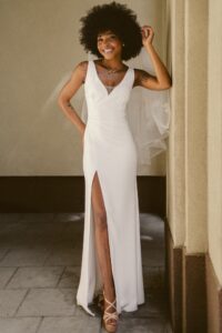 suknia ślubna z dekoltem w serek, długim rozcięciem i tiulowym welonem, modelka w beżowych butach na obcasie