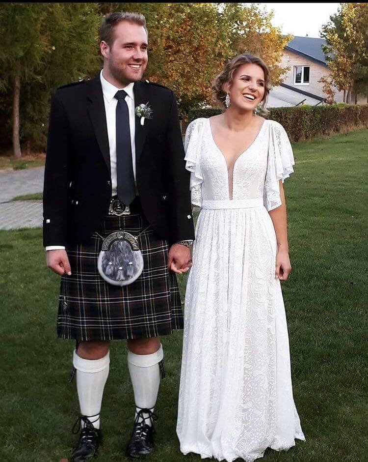 suknia ślubna z dekoltem w serek i rękawami z falbanami, osoba w kiltach trzymająca się za ręce z kobietą