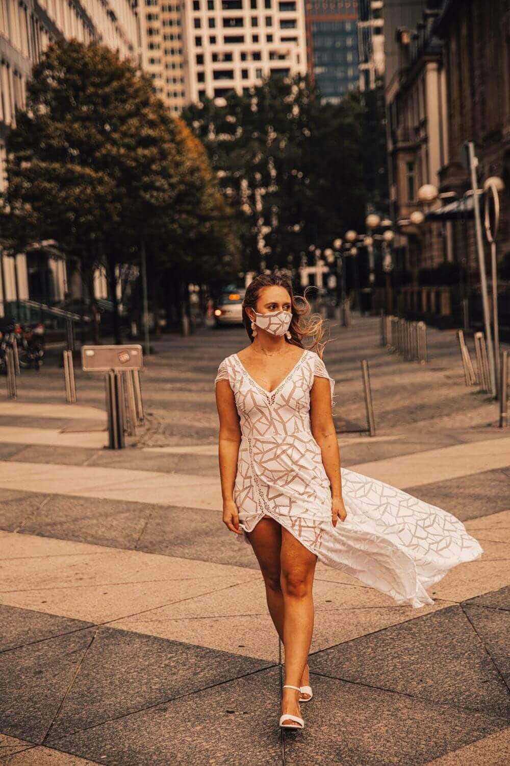 suknia ślubna z koronkowym wzorem i długim trenem, modelka na miejskiej ulicy w maseczce ochronnej