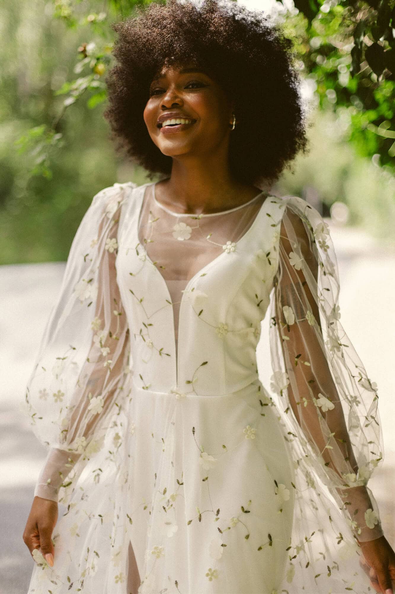 suknia ślubna z przezroczystymi rękawami i haftem w kwiaty, modelka na tle zieleni