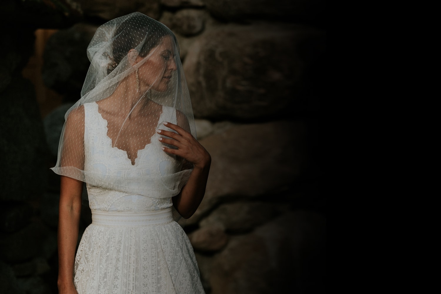 suknia ślubna z koronkowym dekoltem i tiulowym welonem, na tle kamiennej ściany