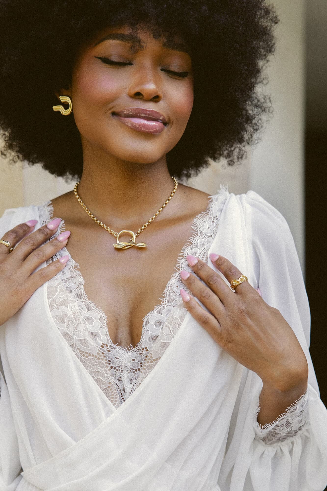 Kobieta w białej sukni z koronkowym dekoltem, nosząca biżuterię na szyi i rękach.