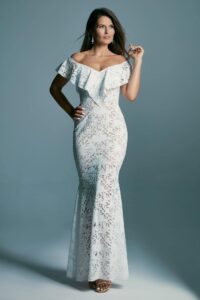 suknia ślubna z koronkowym wzorem, z odkrytymi ramionami i długim krojem, na modelce stojącej na tle szarym