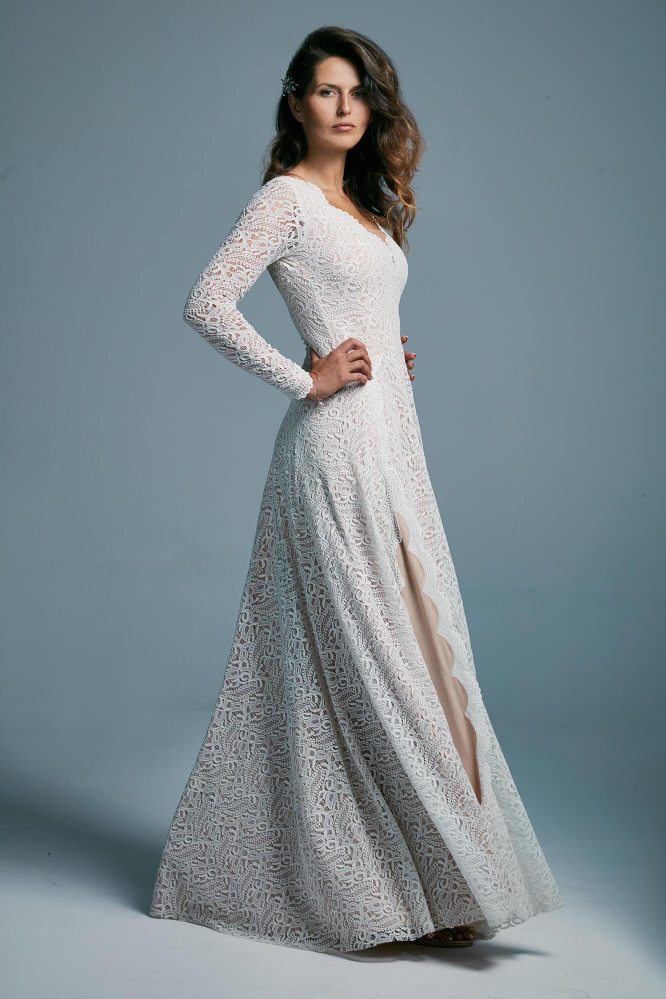 suknia ślubna z długimi rękawami i rozcięciem, w kolorze białym, na modelce stojącej na tle szarym