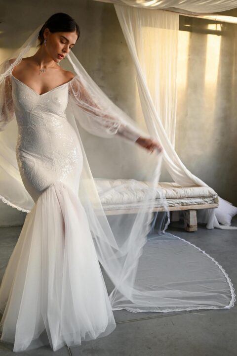 suknia ślubna z długimi rękawami i trenem, z delikatnym welonem w tle