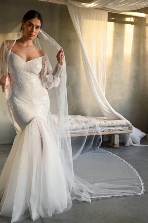 suknia ślubna z koronkowymi rękawami i długim welonem, w tle widoczna sofa i delikatne tkaniny