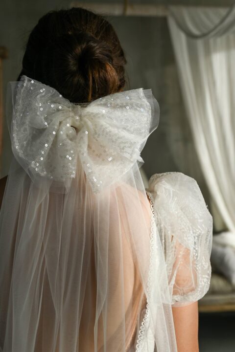 Suknia ślubna z tiulowym trenem i dużą kokardą z ozdobnymi perełkami.