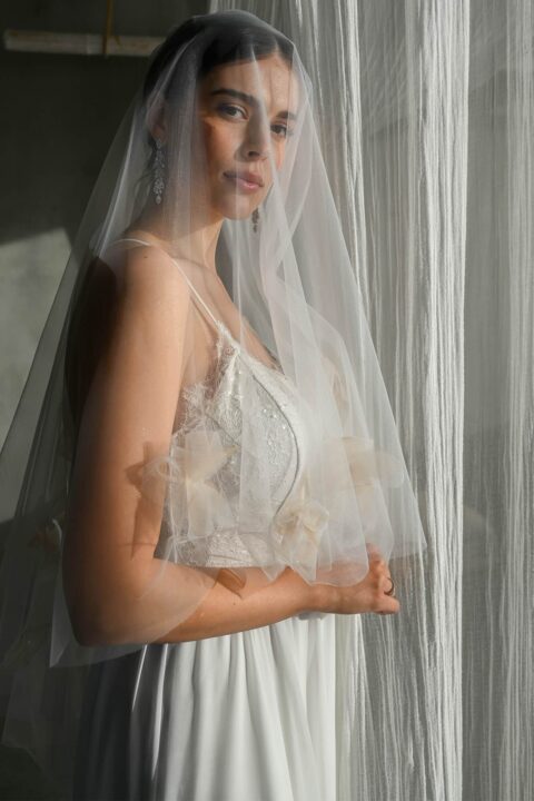 Suknia ślubna z delikatnymi detalami, modelka trzyma welon.