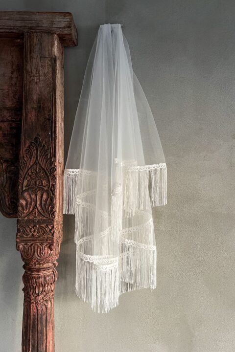 Zasłona ślubna wisząca na tle ściany, z frędzlami na dolnej krawędzi.