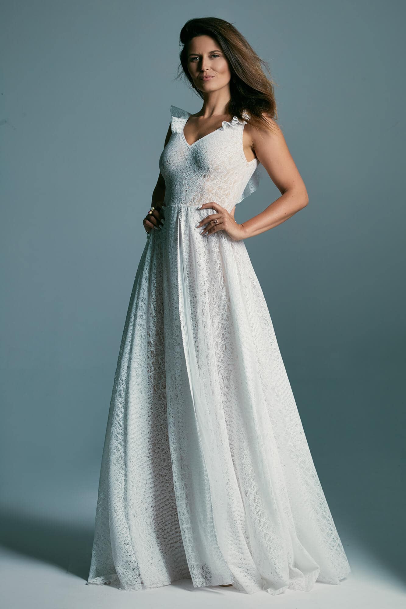 suknia ślubna z długim dołem i ramiączkami, w kolorze białym, na modelce stojącej na szarym tle